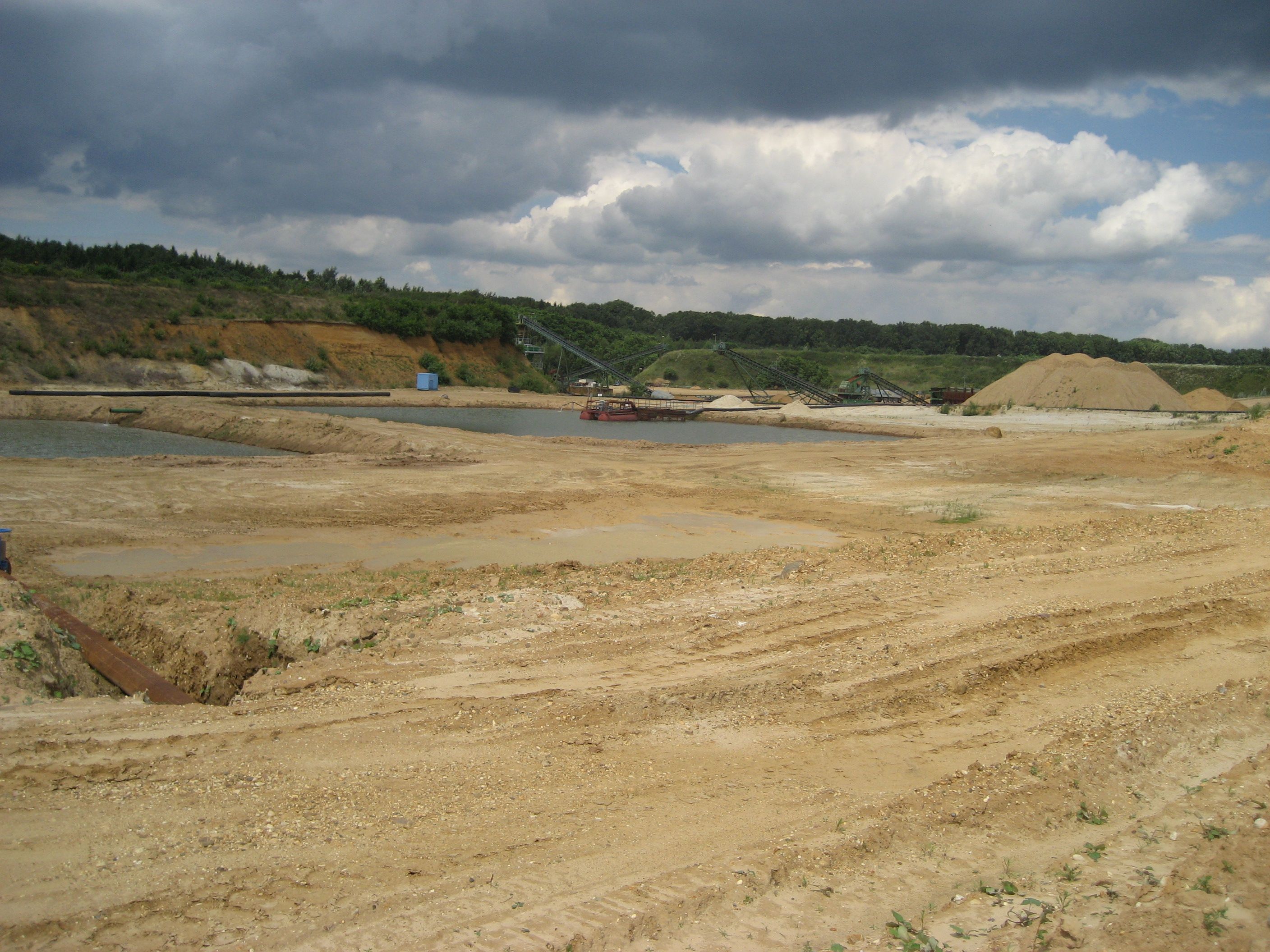 Eine große Sandfläche, Abgrabungsgelände, mit einer Sandbereitungsanalge im Hintergund und Teichanlagen