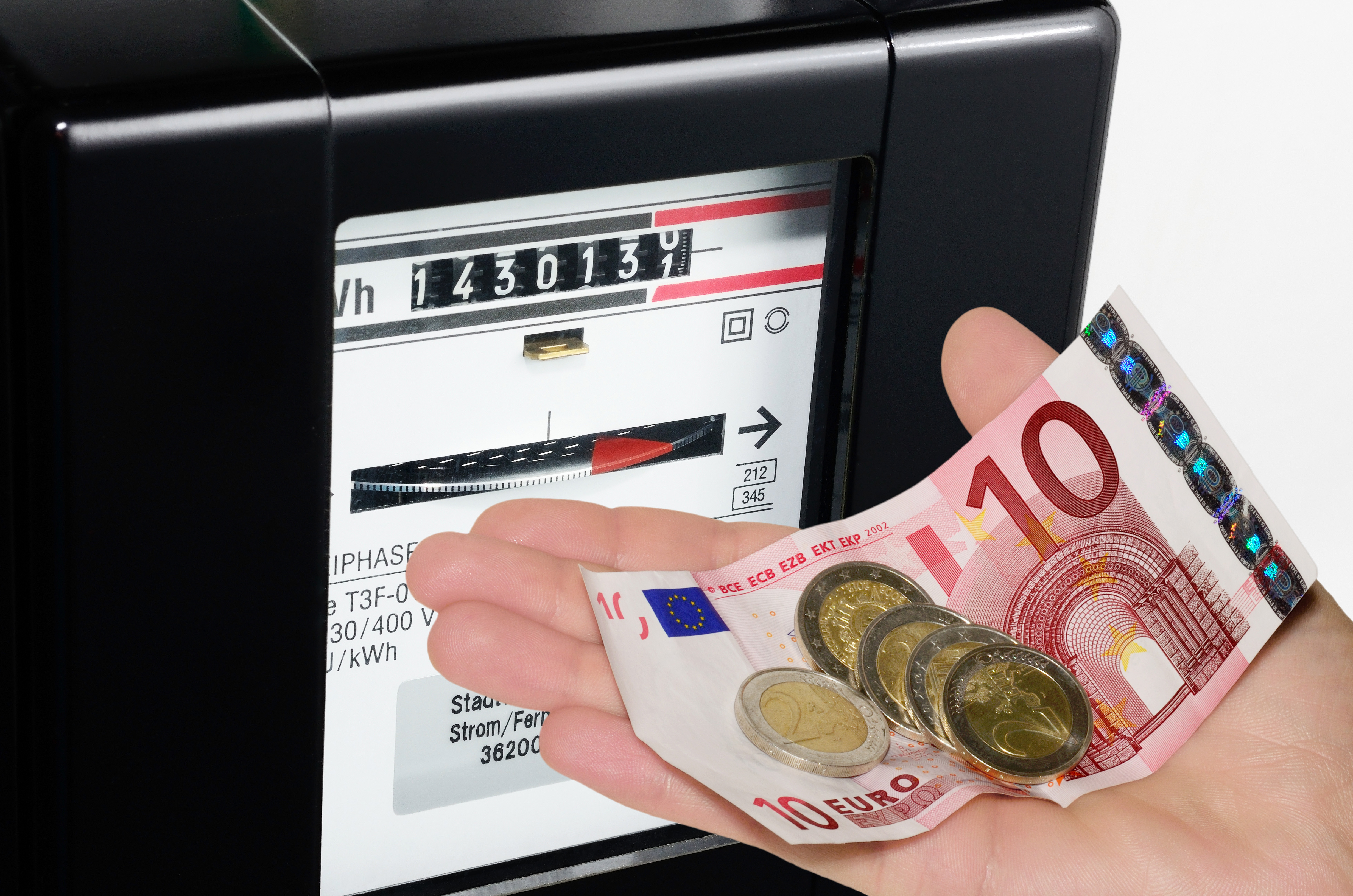 Vor einem Stromzähler hält eine Hand einen 10 Euro Geldschein und Münzen