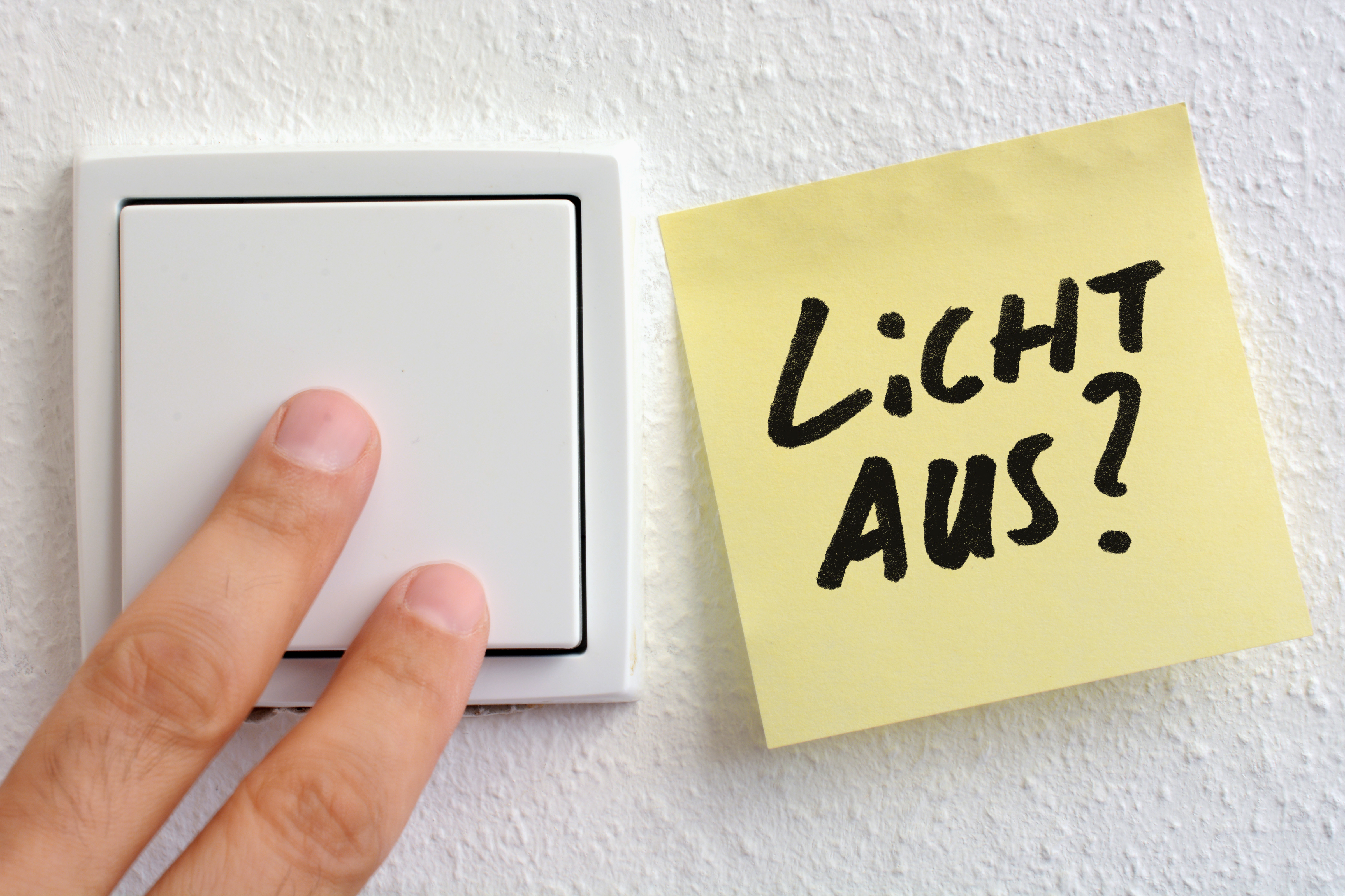 Zwei Finger die einen weißen Lichtschalter drücken und daneben ein Postit mit der Frage "Licht aus?"