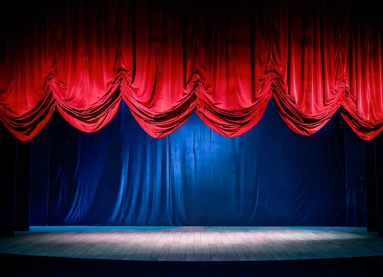 Blick auf eine Theaterbühne mit einem roten, zur Hälft hochgezogenen Vorhang