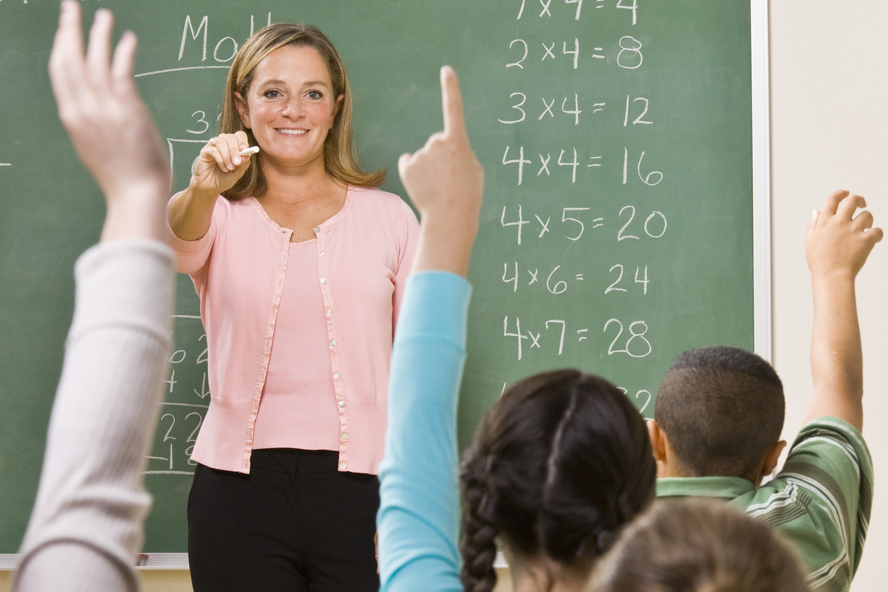 Lehrerin stellt im Klassenraum vor der Tafel Fragen an die Schüler