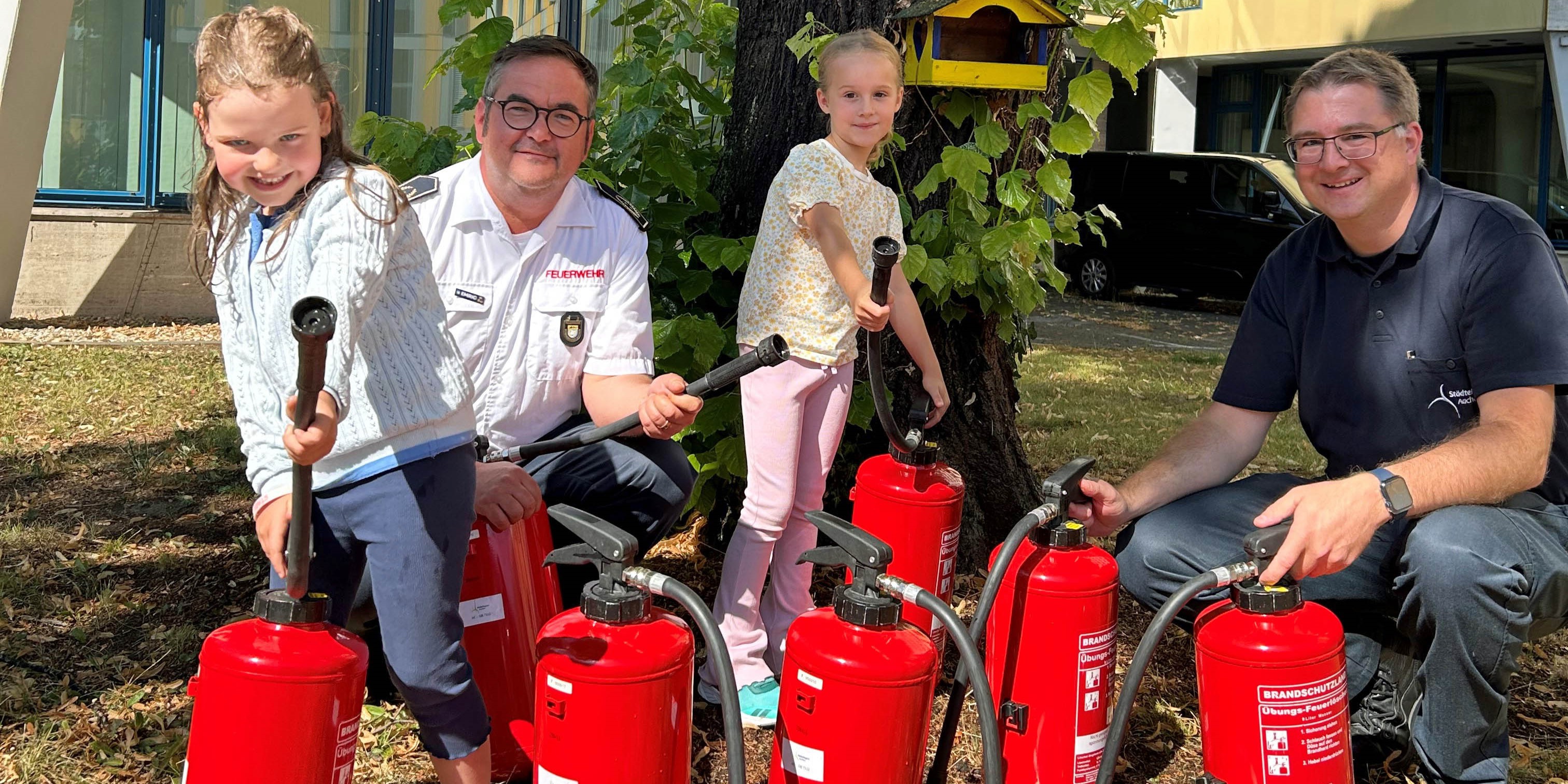 Zwei Mädchen und zwei Feuerwehrmänner mit Feuerlöschern