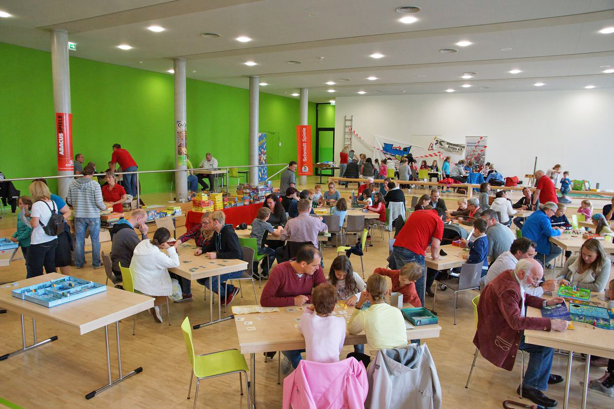 Familien spielen Gesellschaftsspiele an Tischen.