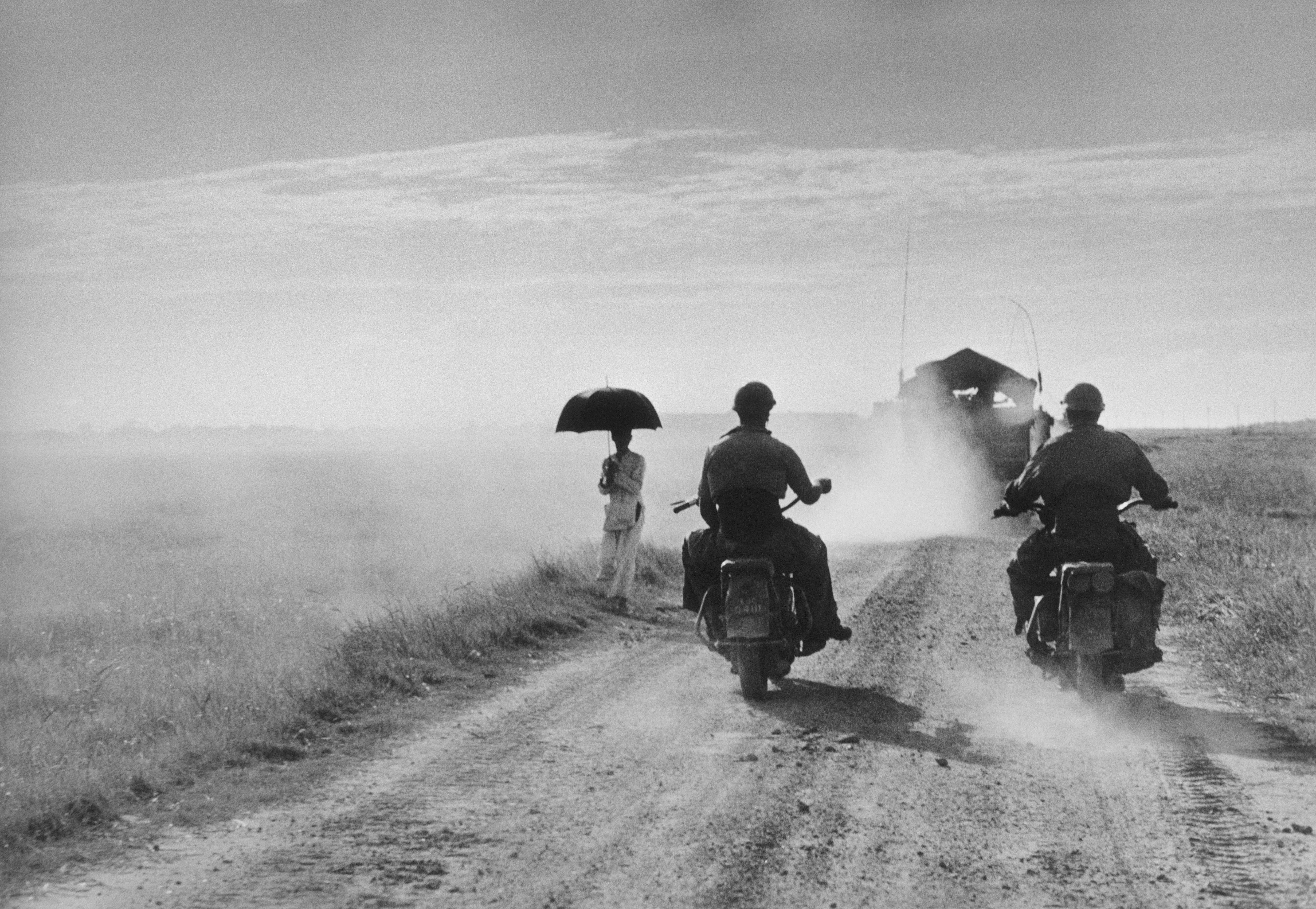 Motorcyclists and woman walking on the road from Nam Dinh to Thai Binh, Indochina (Vietnam), May, 1954. 